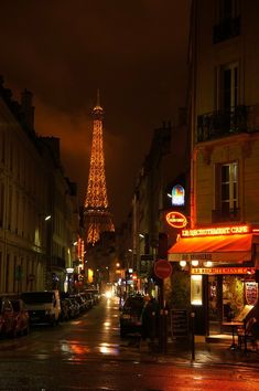 the eiffel tower is lit up at night, with people walking down the street