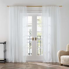 a white chair sitting in front of a window next to a wooden floor and door