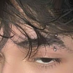 a close up of a person's face with black hair and piercings on his forehead