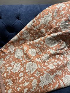 an orange and white flowered comforter sitting on top of a blue velvet couch