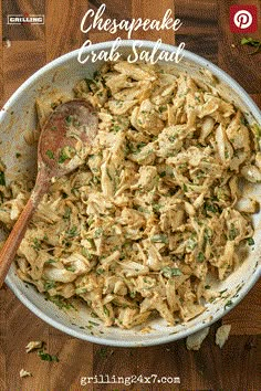 a white bowl filled with chicken salad on top of a wooden table next to a spoon