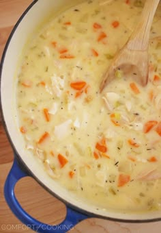 a pot filled with chicken and carrots on top of a wooden table next to a spoon