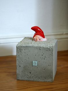 there is a small gnome sitting on top of a cement block with a red hat