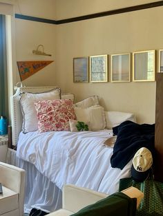 a white bed sitting next to a window in a room with pictures on the wall