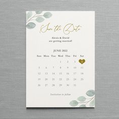 save the date card with gold foil leaves and hearts on it, in front of a gray background