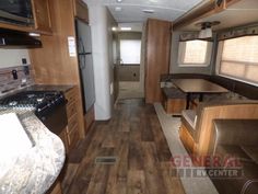 the interior of an rv with wood flooring and leather couches, kitchenette, stove top oven, microwave and refrigerator