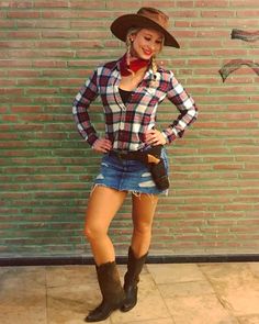 a woman standing in front of a brick wall with her hands on her hips and wearing cowboy boots