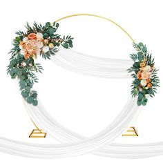 a wedding arch decorated with flowers and greenery on white fabric draped in gold metal stand