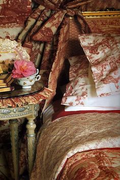 a table with a flower on it next to a bed covered in red and gold sheets