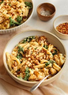 two bowls filled with pasta and vegetables on top of a white table cloth next to some seasoning