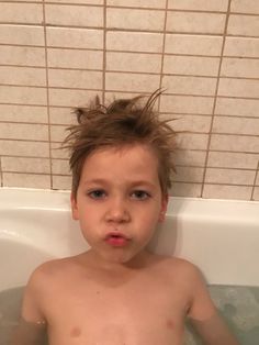 a young boy sitting in a bathtub with no shirt on