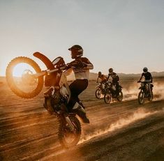 several people riding dirt bikes on a dusty road at sunset with the sun behind them