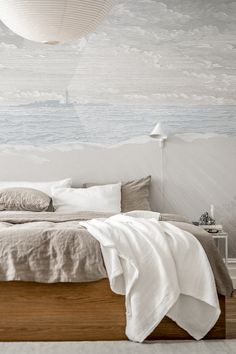 a bed with white sheets and pillows on it in front of a wall mural that looks like the ocean