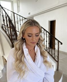 a woman with long blonde hair standing in front of a stair case and looking down at her phone