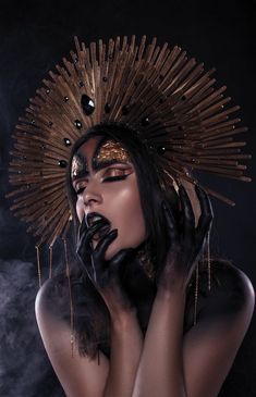 a woman with her hands on her face, wearing black and gold makeup art work