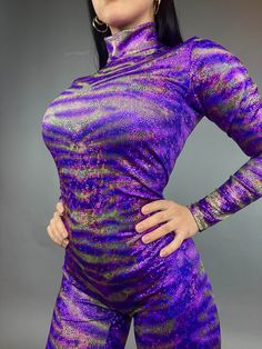 The Avatar Purple Catsuit is a striking and versatile piece designed for aerialists, contortionists, and performers. This full-body catsuit features a vibrant purple color with a holographic metallic pattern print that shimmers under the lights. It includes a turtleneck, long sleeves, and long legs, with a back zipper for convenient dressing. Captivating Color: The vibrant purple hue and holographic print create a mesmerizing effect that's perfect for stage performances. Versatile Design: Ideal Catsuit Bodysuit, Catsuit Costume, Bodysuit Costume, Metallic Pattern, Cup Sleeve, Vibrant Purple, 4 Way Stretch Fabric, Full Sleeves, Catsuit