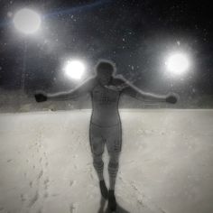 a person standing in the snow with their arms spread out and lights on behind them