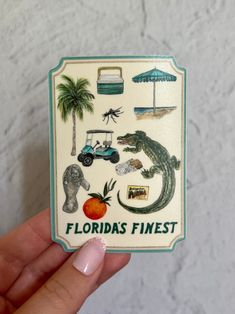 someone holding up a florida finest sticker in front of a white marble wall with palm trees and alligators on it