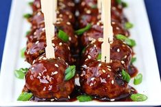 several skewered meatballs with sauce and garnish on a white plate