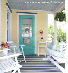 the front porch is decorated with white rocking chairs and bright blue door, along with potted plants