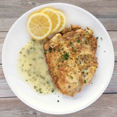 a white plate topped with meat and gravy next to a slice of lemon