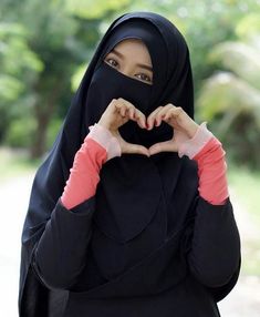 a woman wearing a black hijab making a heart shape with her hands in front of her face