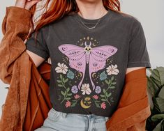 Embrace your mystical side with this Luna Moth Mystic Moon Flowers Shirt! This Celestial Cottagecore Shirt is perfect for green witches and goblincore enthusiasts alike. With a touch of boho flair, this Comfort Colors Boho Vintage Tee features a stunning moon design that will appeal to Luna moth Shirt collectors. Add a dash of magic to your wardrobe with this Mystical Moon Tee that doubles as a Spiritual T-Shirt. Treat yourself or gift this Witch Shirt to a friend as a unique and enchanting pres Halloween Fairy Grunge Festival Tops, Fairy Grunge Halloween Festival Tops, Fairy Grunge Tops For Halloween Festival, Black Bohemian Tops For Halloween, Black Bohemian Top For Halloween, Casual Halloween Festival T-shirt, Fairy Grunge Crew Neck T-shirt For Festival, Celestial Cottagecore, Moth Shirt