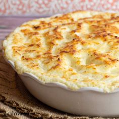 a white dish filled with cheese on top of a wooden tablecloth next to a fork