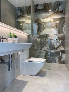 a white toilet sitting next to a bathroom sink under a glass shower door in front of a mirror