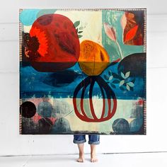 a person standing in front of a painting holding up a large piece of art that has been painted on it