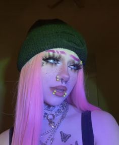 a woman with pink hair and piercings on her face wearing a green beanie