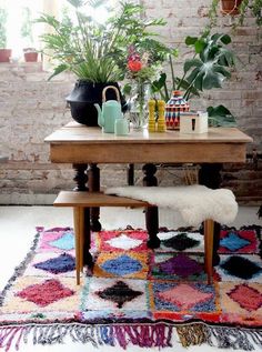 a wooden table sitting on top of a colorful rug next to a plant filled wall