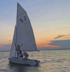 two people on a small sailboat in the ocean at sunset or dawn with one person raising their arms up