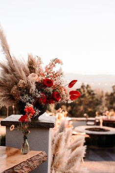 a vase filled with flowers sitting on top of a wooden table next to tall grass