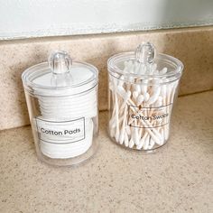 two clear containers filled with cotton swabs next to each other on a counter