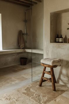 a wooden stool sitting in front of a bath tub next to a window and tiled floor