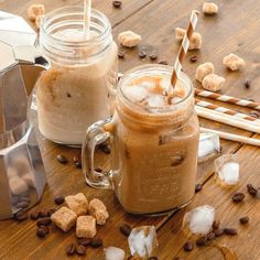 two mugs filled with iced coffee on top of a wooden table next to sugar cubes