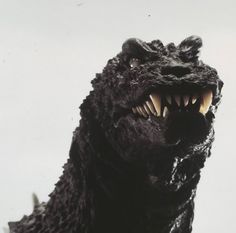 a close up of a fake godzilla head on a white background with the mouth open