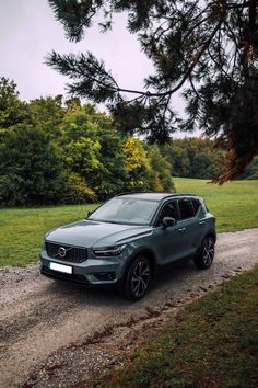 a grey volvo suv parked on the side of a dirt road next to a tree