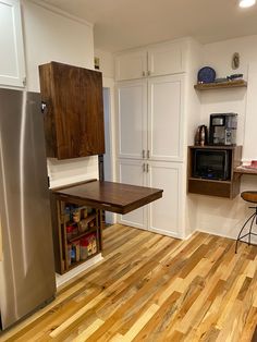 a kitchen with wooden flooring and white cupboards next to a silver refrigerator freezer