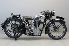 an old fashioned motorcycle is parked on the cement floor in front of a white wall