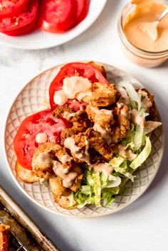 a white plate topped with lettuce and tomatoes next to some dipping sauces