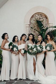 a group of women standing next to each other in front of a white building holding bouquets