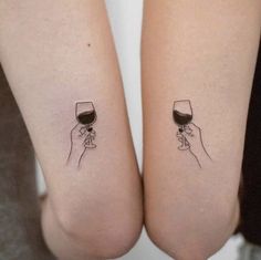 two people holding wine glasses on their legs with the same tattoo design on their arms