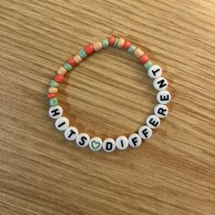 a beaded bracelet with words written in white and green beads on a wooden surface