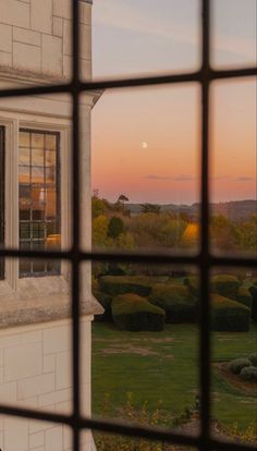 the view from behind a window looking out onto a lawn and bushes at sunset, with an orange moon in the distance