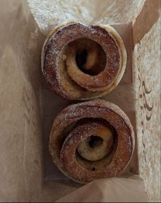 two doughnuts sitting in a box with powdered sugar on them