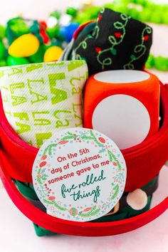 a red basket filled with lots of different types of christmas decorations and paper tags on top of it