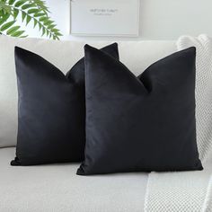 two black pillows sitting on top of a white couch next to a potted plant