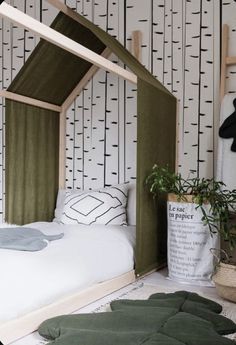 a bed with a green canopy over it in a room that has trees on the wall